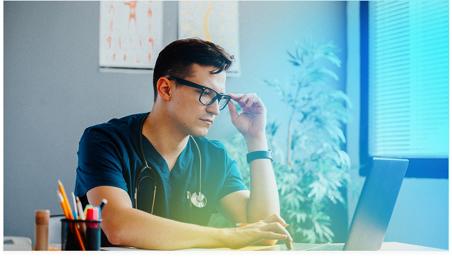 A clinician at his desk reviewing work on a laptop